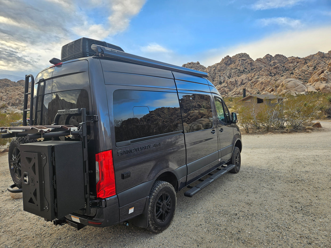Rugged dark grey 4x4 camper van, ideal as an rv rental, ready for desert adventures amidst rocky landscapes.