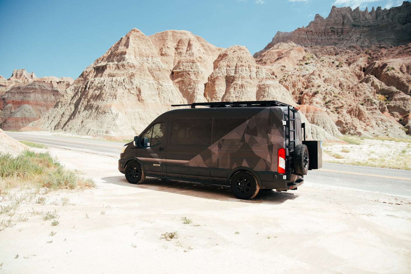 Adventure-ready rv rental: A custom geometric-patterned camper van is parked on a sandy shoulder amidst majestic Badlands peaks.