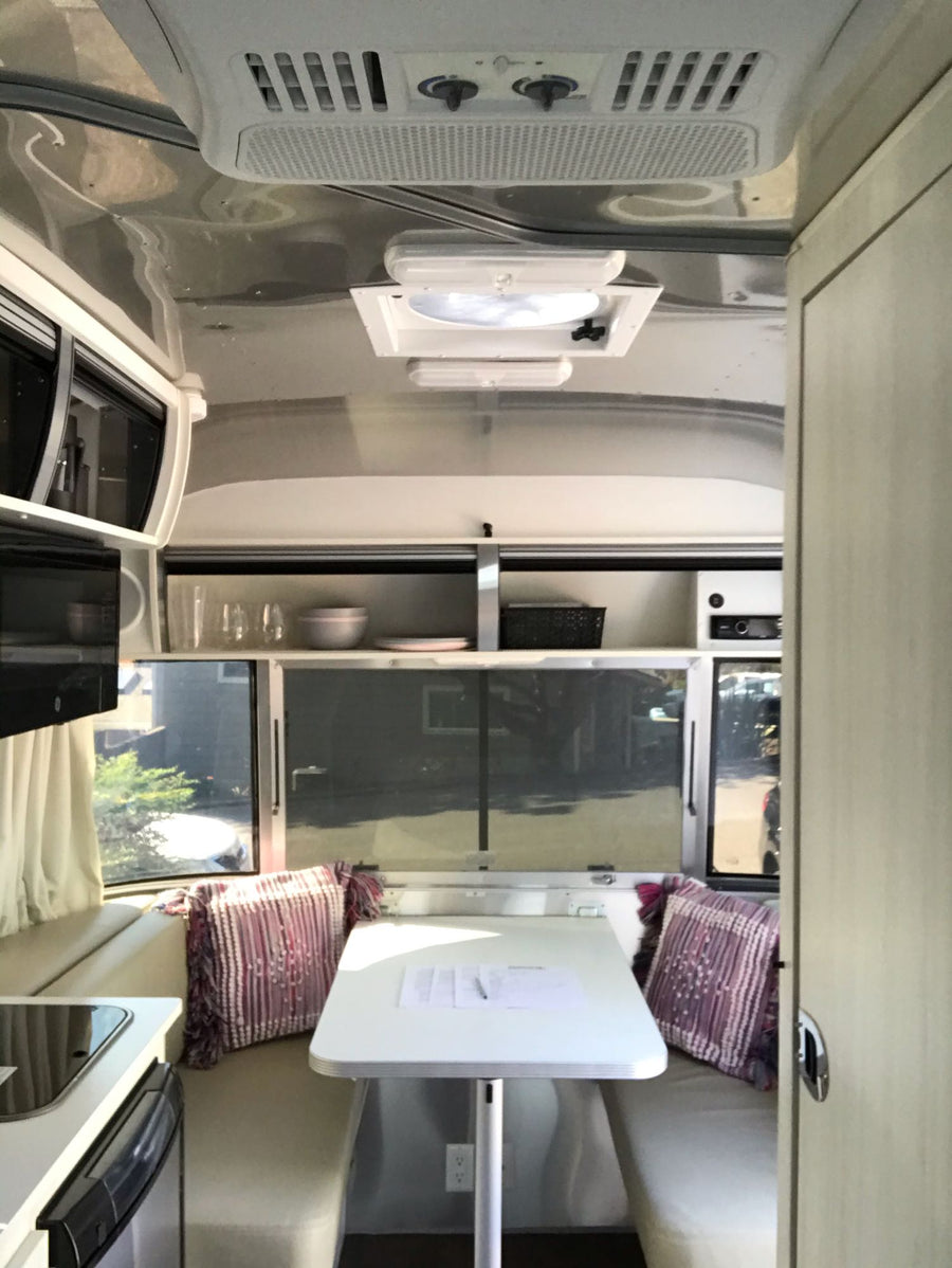and large windows revealing parked vehicles outside.|Cozy Airstream RV rental bedroom with gray bedding