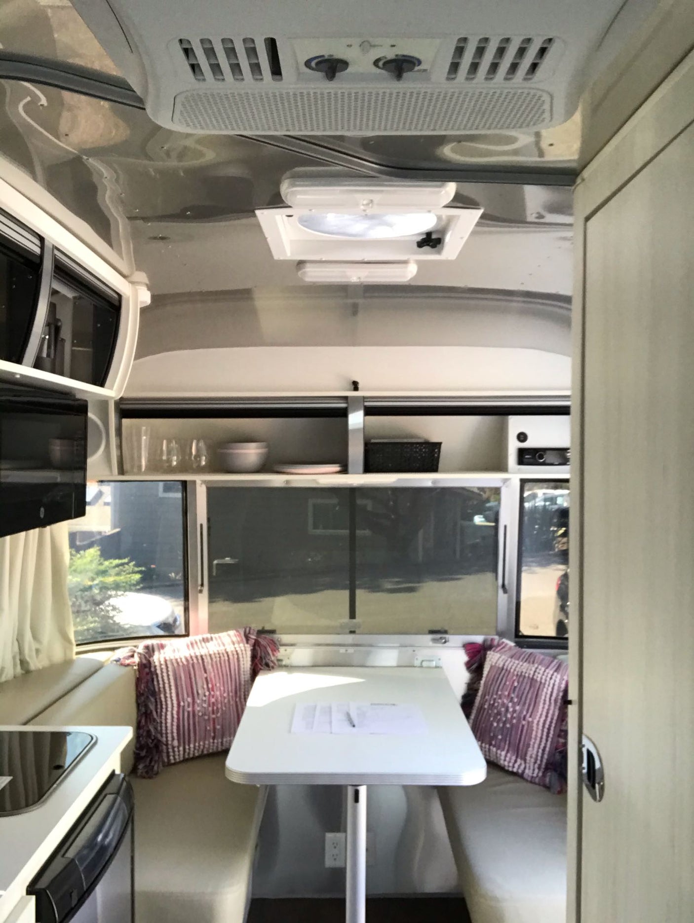 and large windows revealing parked vehicles outside.|Cozy Airstream RV rental bedroom with gray bedding