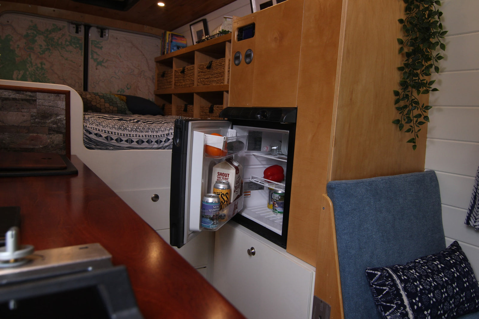Cozy rv rental interior with an open fridge, comfy bed, map-lined walls, and clever storage. Ready for your next van life trip!
