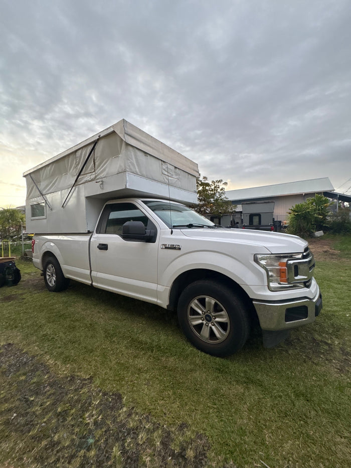 parked in a sunny driveway with palm trees.|White Ford F-150 pickup truck with a pop-up truck bed camper. Great RV rental option.|White Ford truck with a camper shell