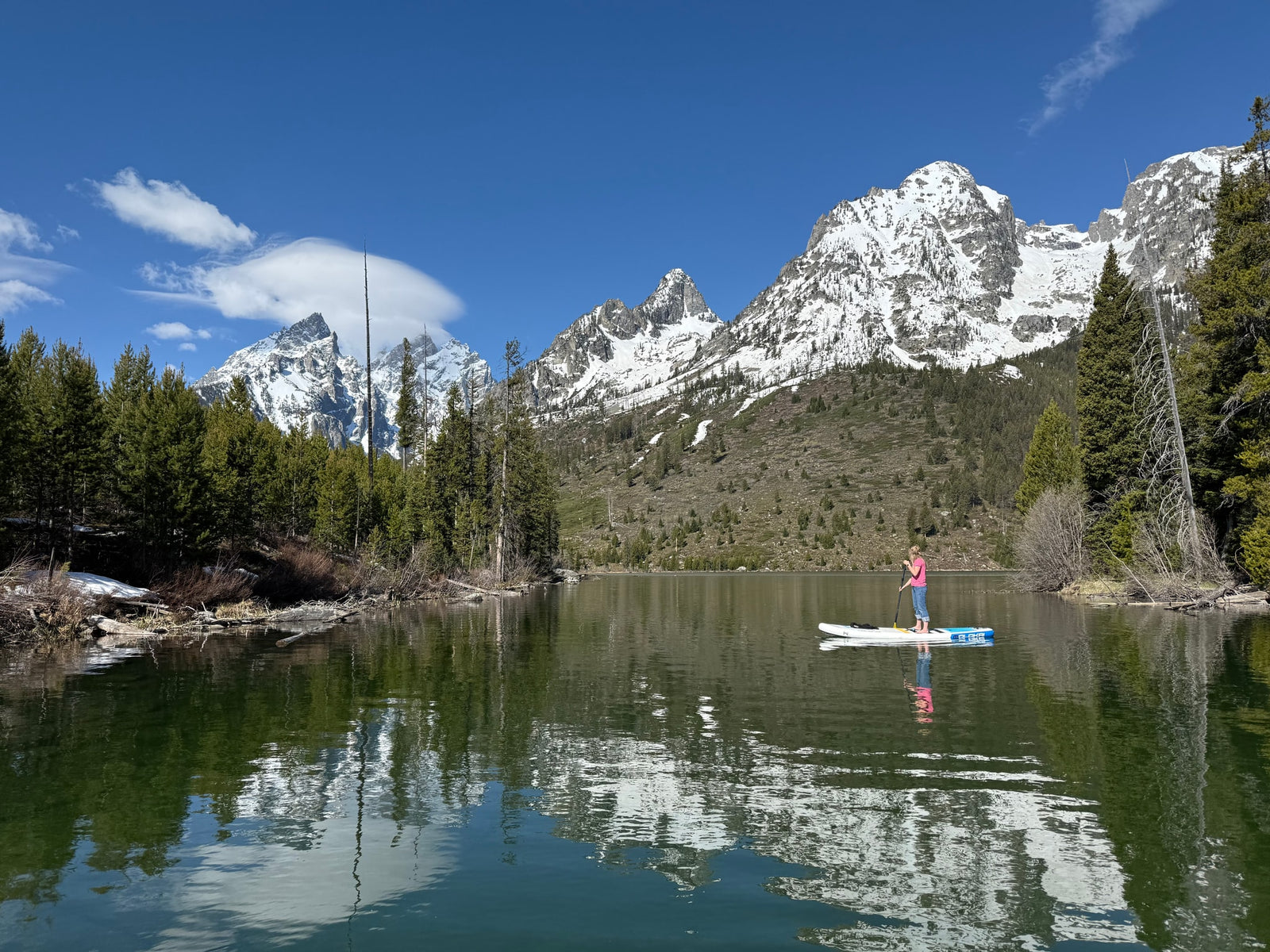 Paddleboarder on a clear mountain lake, snowy peaks reflecting. Ideal RV rental destination!