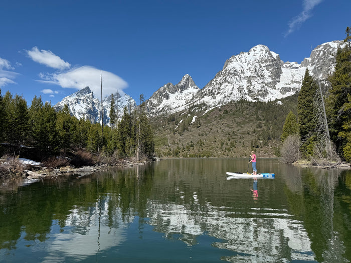 Paddleboarder on a clear mountain lake, snowy peaks reflecting. Ideal RV rental destination!