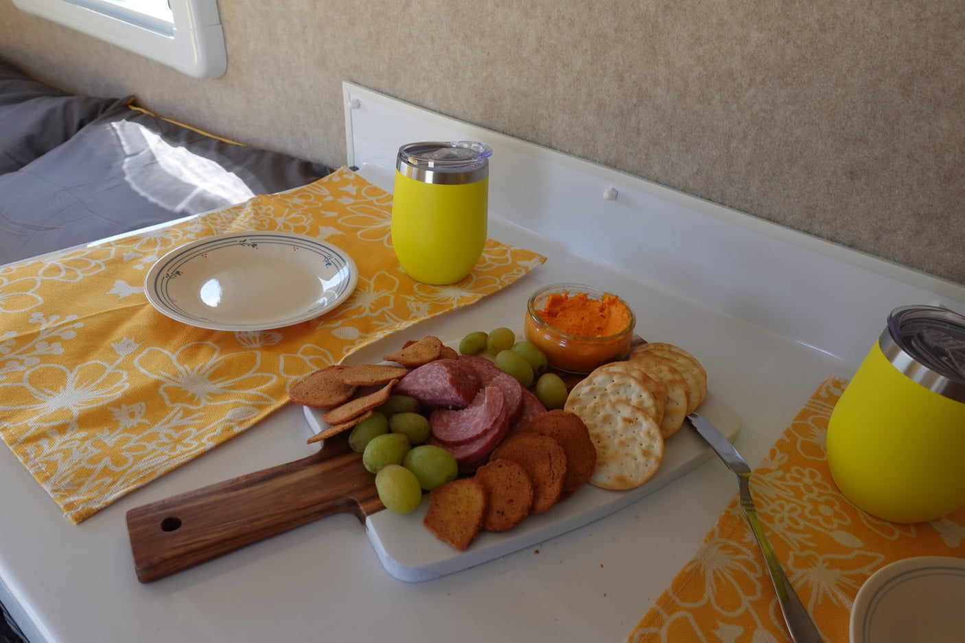 Enjoying a charcuterie board with salami, crackers, grapes, and dip in an RV rental. Yellow cups and placemats add cheer.