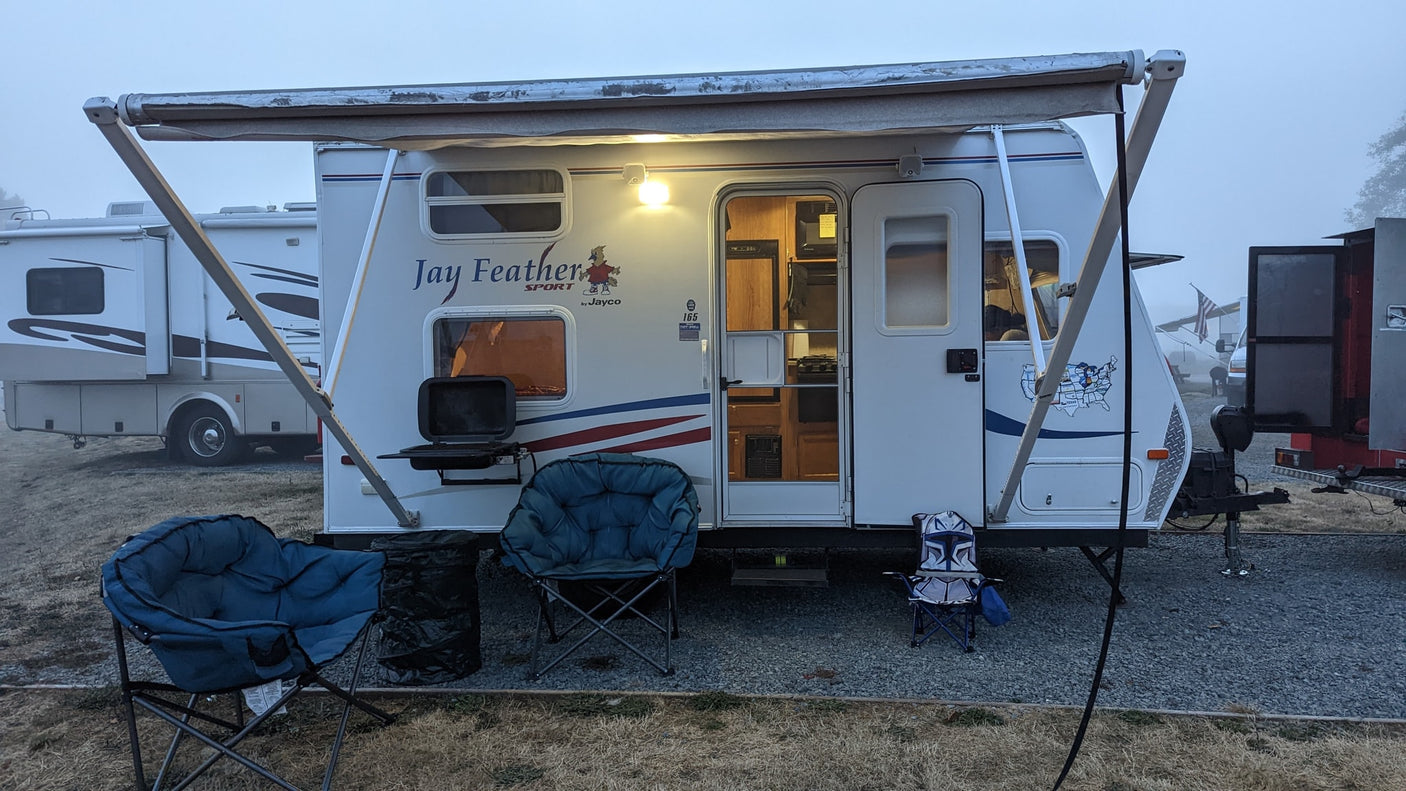 This RV rental, a Jay Feather travel trailer, is set up for camping with an awning, chairs, and grill, providing cozy outdoor living.