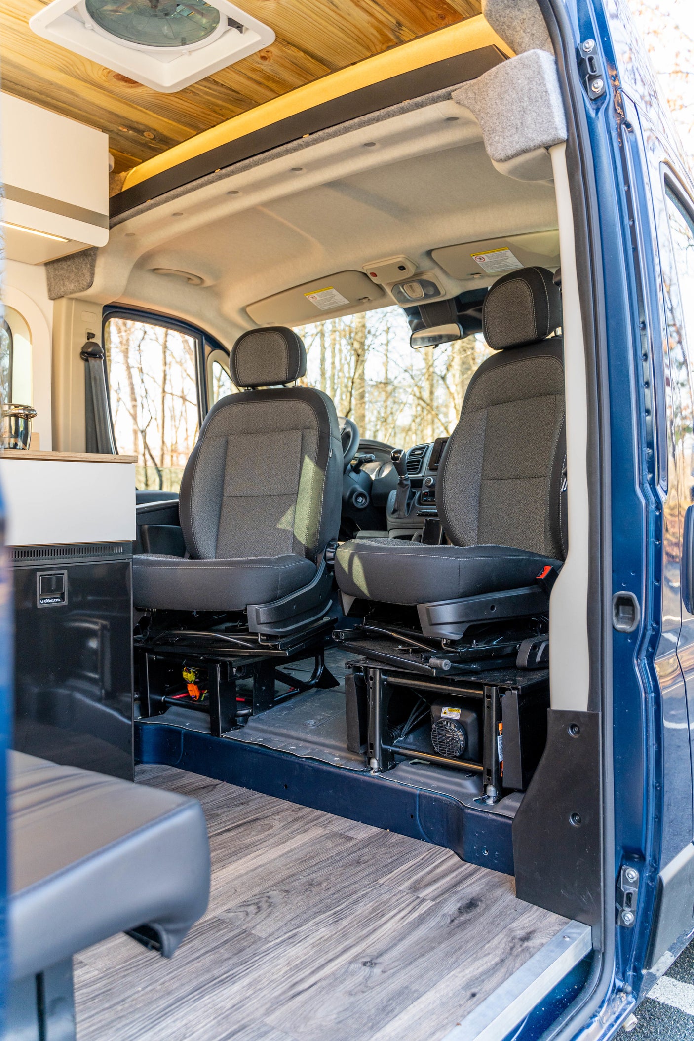 Inside an RV rental van: The customized front cabin features swivel seats, wood-paneled ceiling, and light wood-look floor.