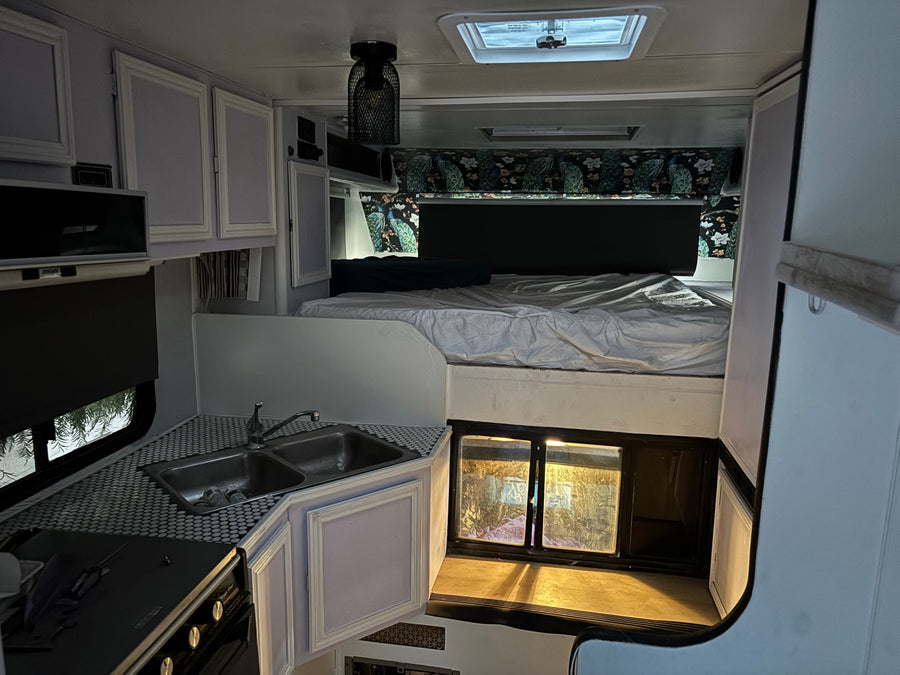 Cozy RV rental interior featuring a compact kitchen with sink and stove, raised bed, overhead cabinets, and a skylight.