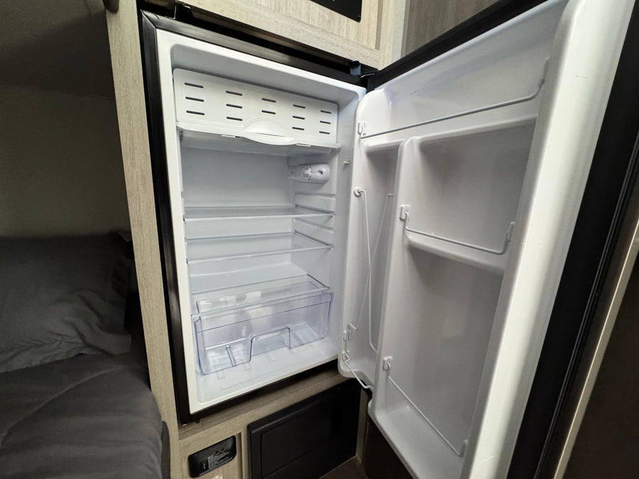 This RV rental features a clean, open mini-fridge with shelves and door storage, ready for your travel essentials.