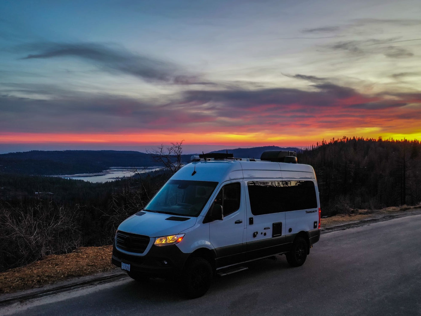 This white camper van enjoys a vibrant sunset over a lake. Perfect for your next scenic RV rental adventure!
