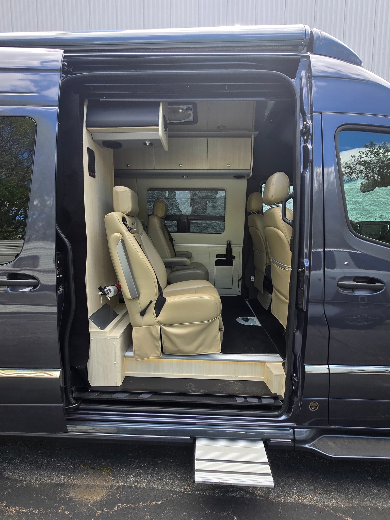 Open side of an rv rental camper van, revealing tan leather seats, wood cabinetry, and an extended step for access.