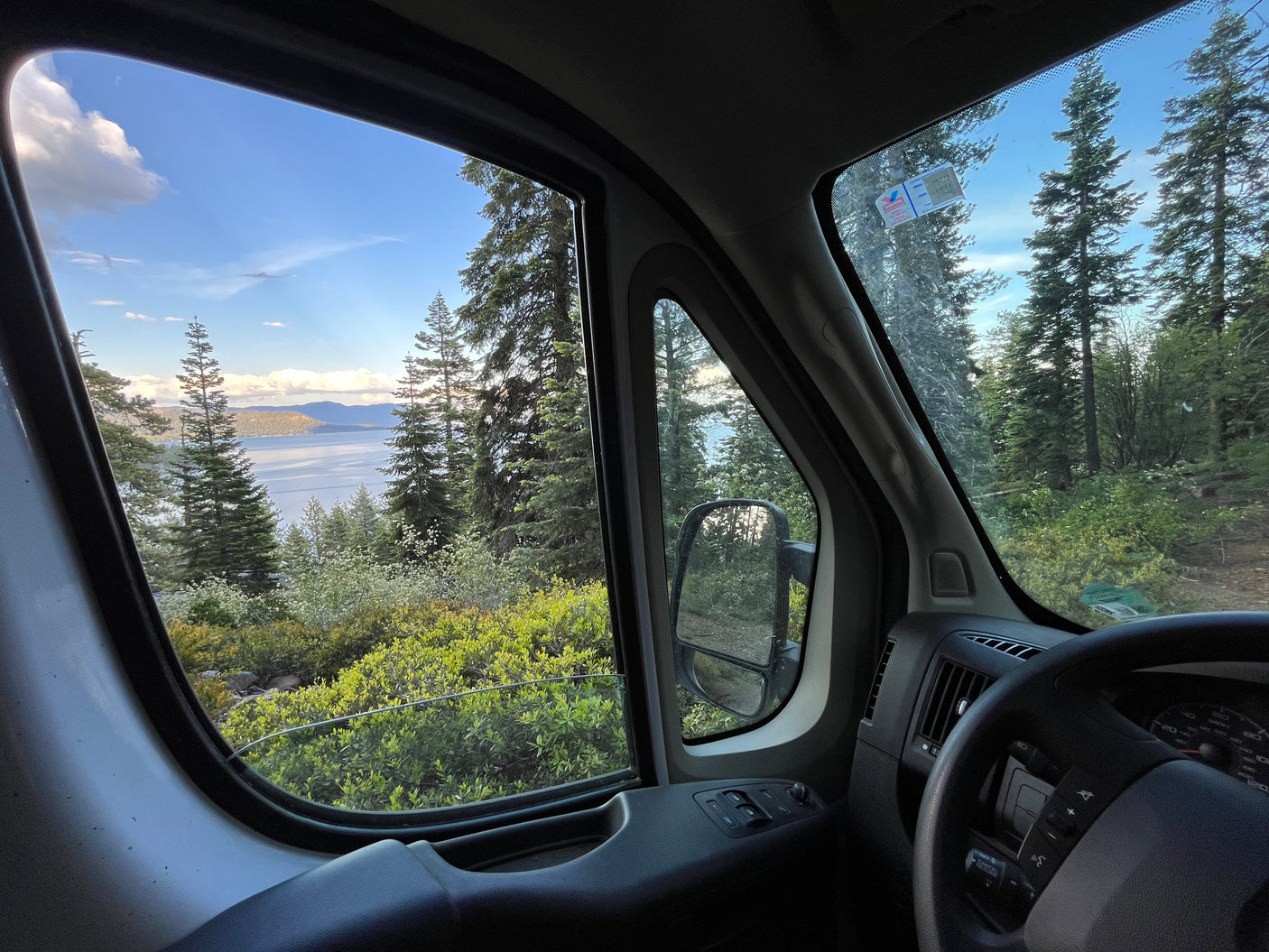 Inside an RV rental: a serene lake view with surrounding forest, seen from the driver's window.