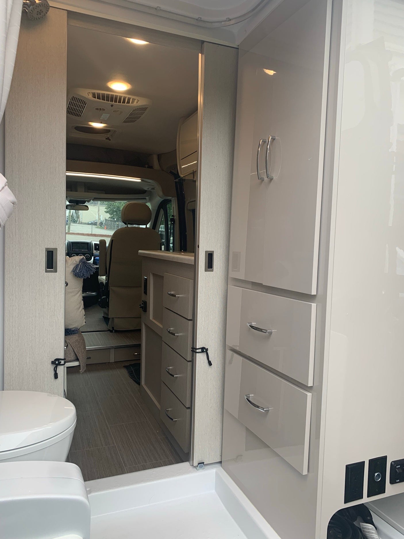 Modern RV rental interior: compact bathroom with shower, sliding door to living area & cockpit.