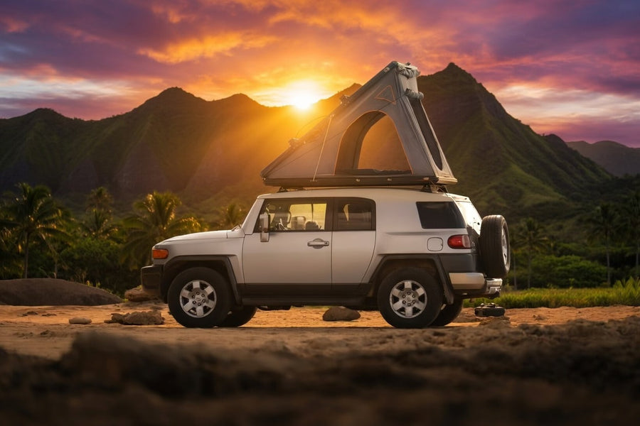with mountains & palms. Explore like this with an RV rental!|RV rental adventure! Silver Toyota FJ Cruiser with a rooftop tent by a majestic waterfall and green mountains.|An FJ Cruiser with a rooftop tent