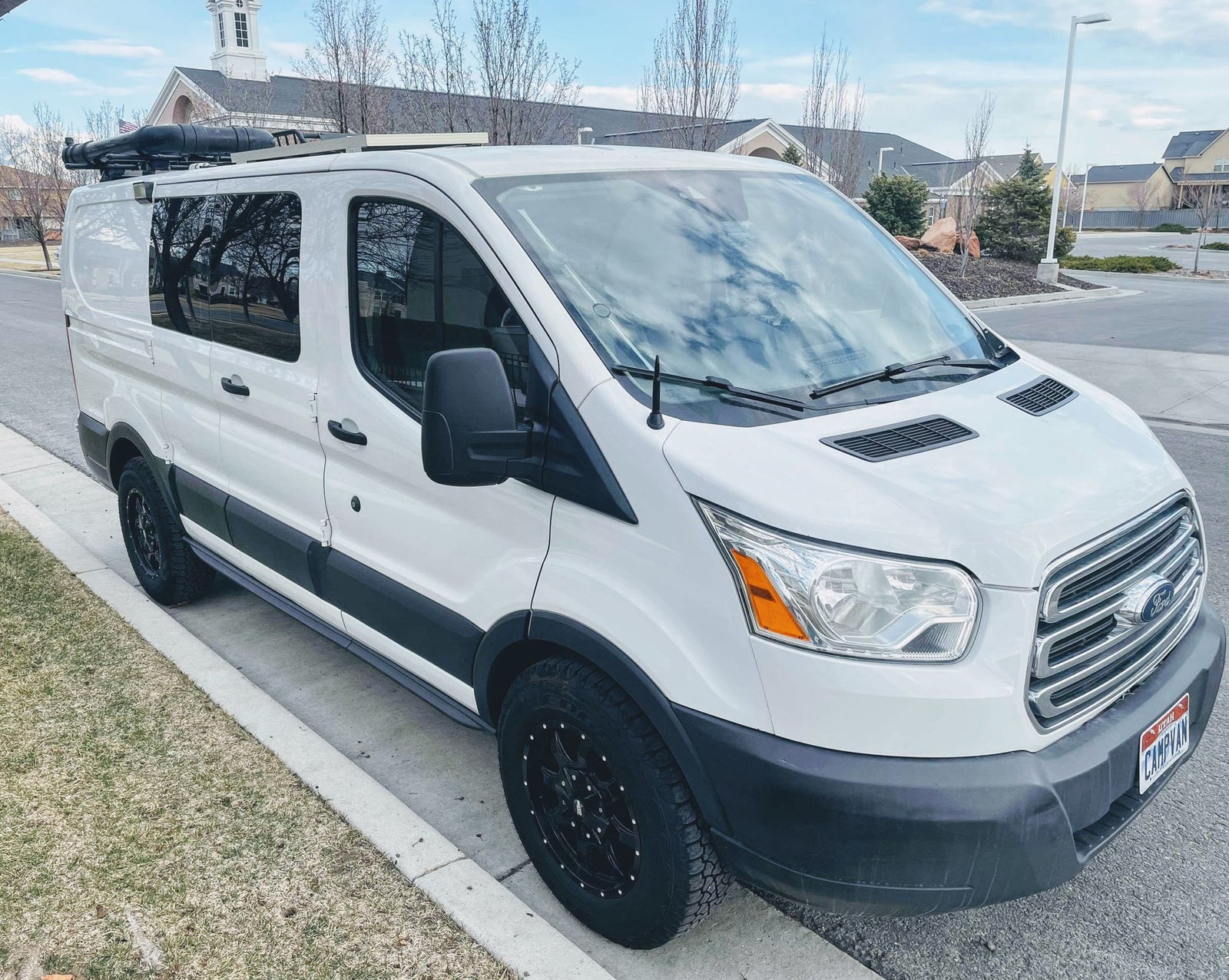 Front 3/4 view of a white Ford Transit camper van with custom tires and roof rack