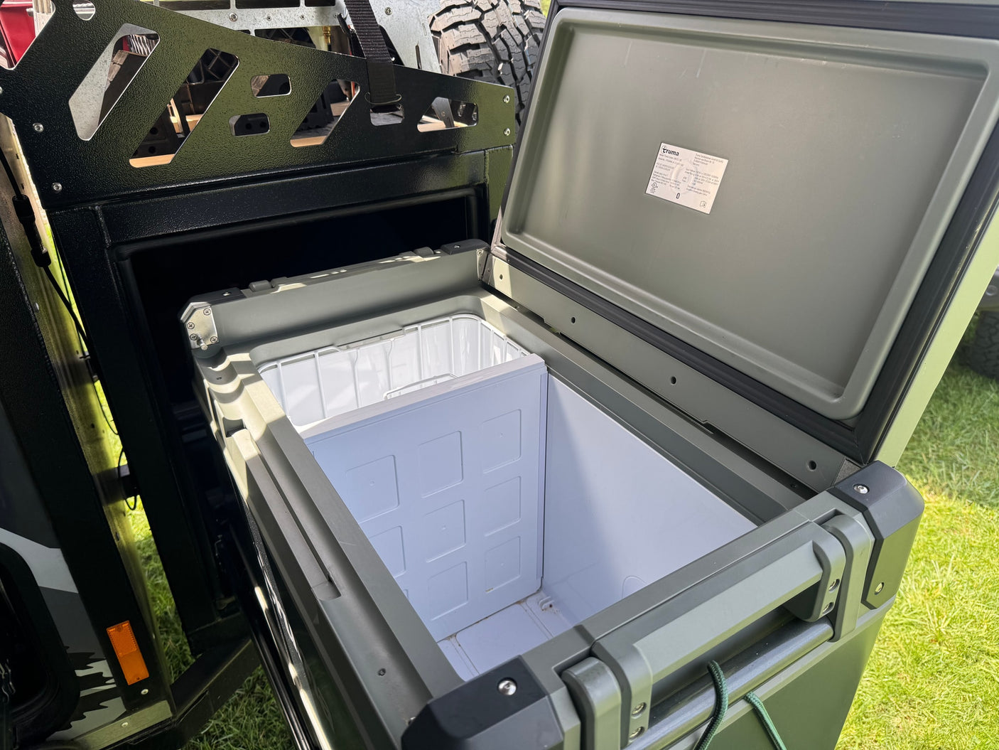 Open, olive-green Truma portable fridge/cooler, installed in an outdoor RV rental setup.