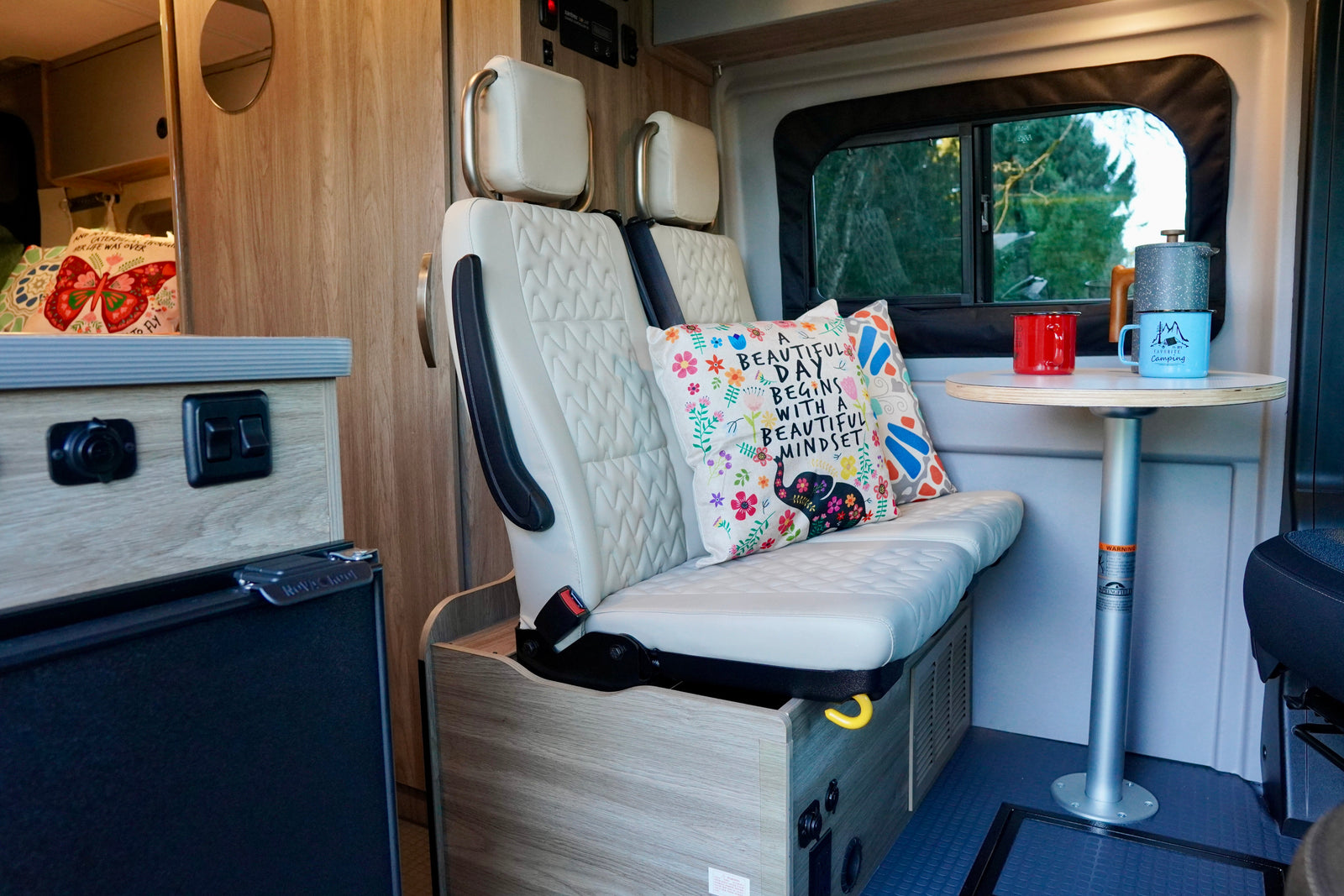 Relax in your RV rental! This camper van features cozy interior seating, a dining table, and a scenic window view for your travels.