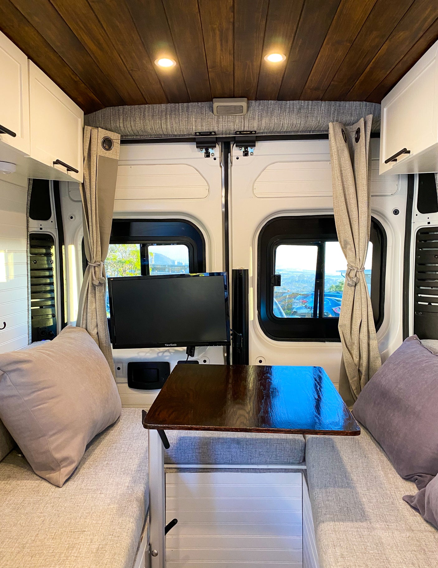 This cozy RV rental interior features a wood ceiling, TV, table, and comfy bench seating for travel comfort.