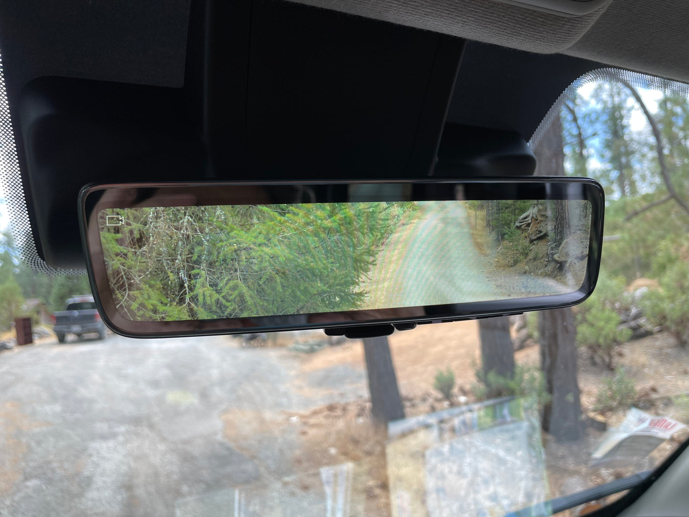 An RV rental's digital rearview mirror displays a rear camera view of a wooded path, enhancing driving visibility.