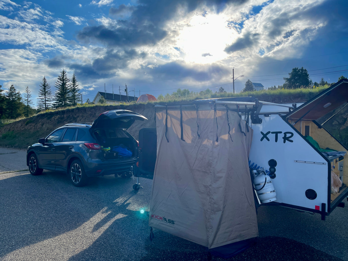 SUV & XTR teardrop trailer RV rental setup with an outdoor shower tent, ready for camping under a bright sky.
