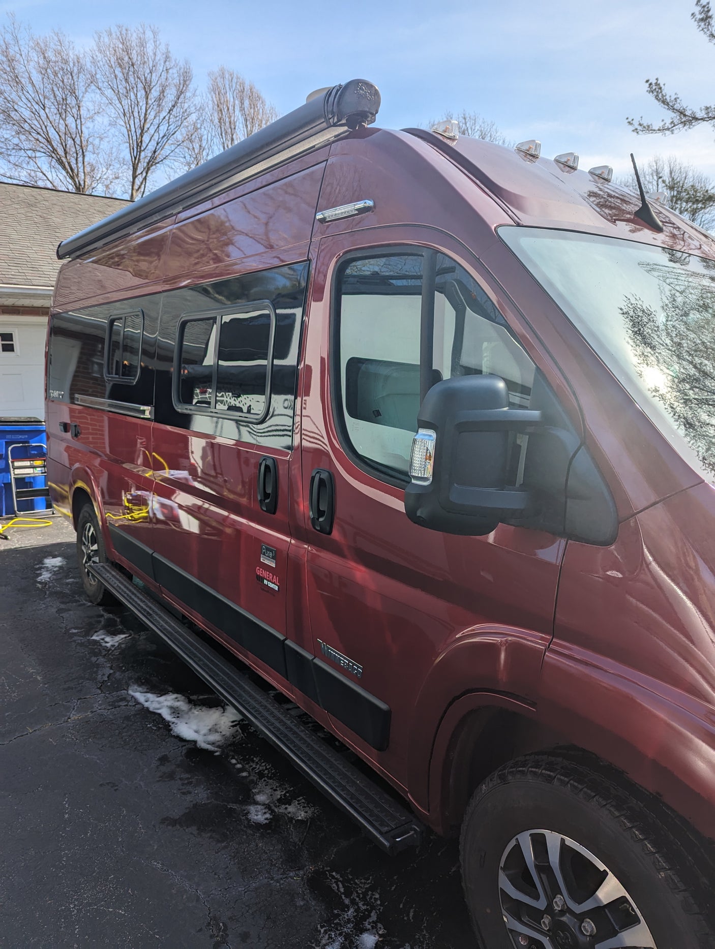 A maroon Winnebago camper van, seen from the side, features a mounted awning and roof lights. Ideal for RV rental.