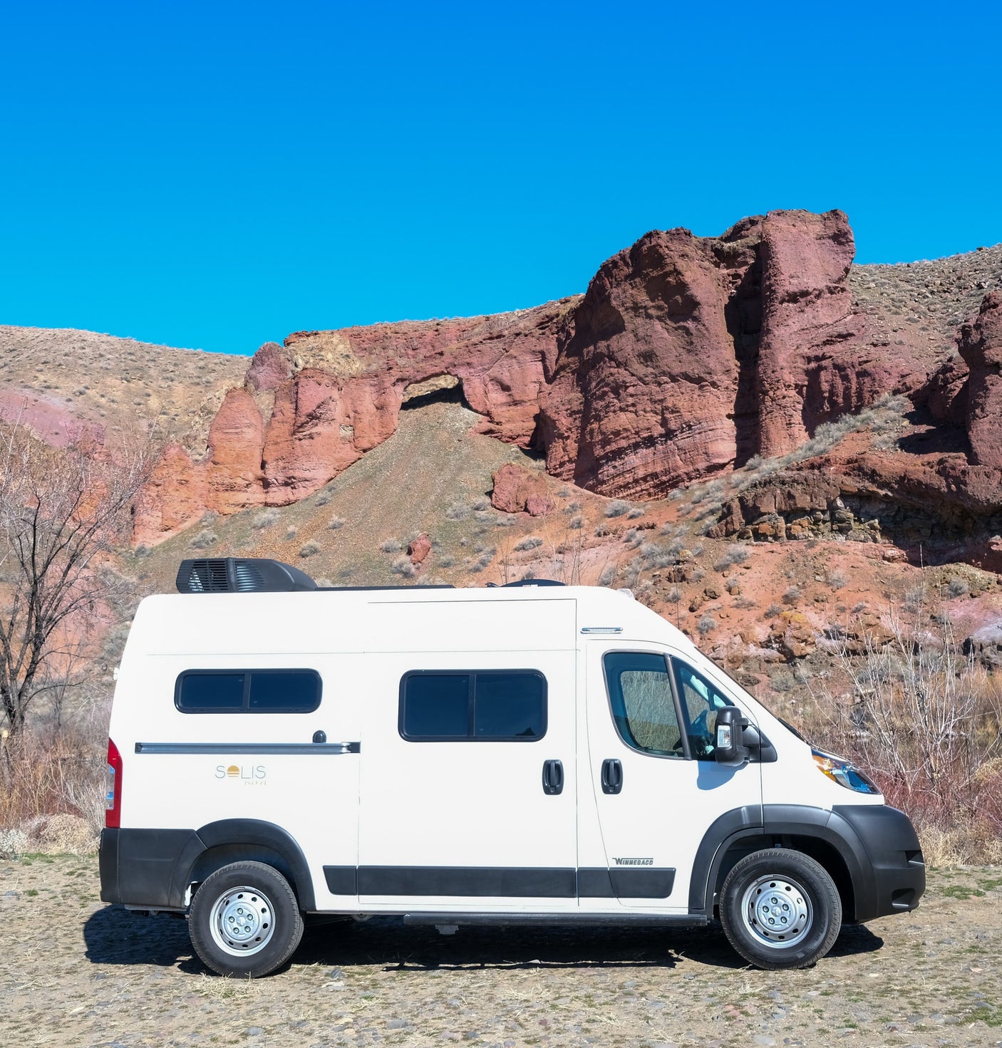 White Winnebago Solis rv rental parked against stunning red rock formations under a clear blue sky, perfect for adventure.