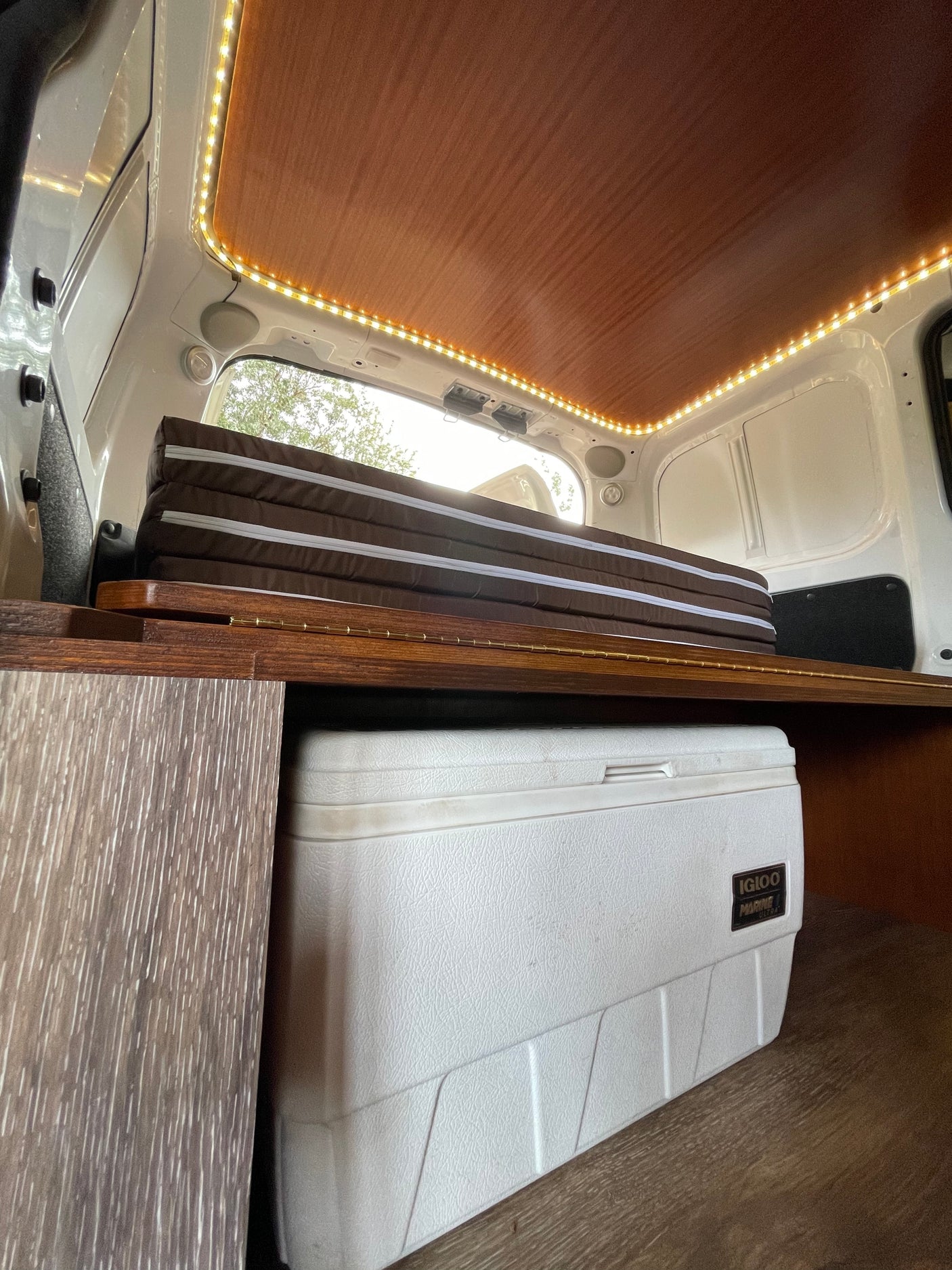 Cozy RV rental interior with folding mattress, cooler storage, and warm LED lighting.