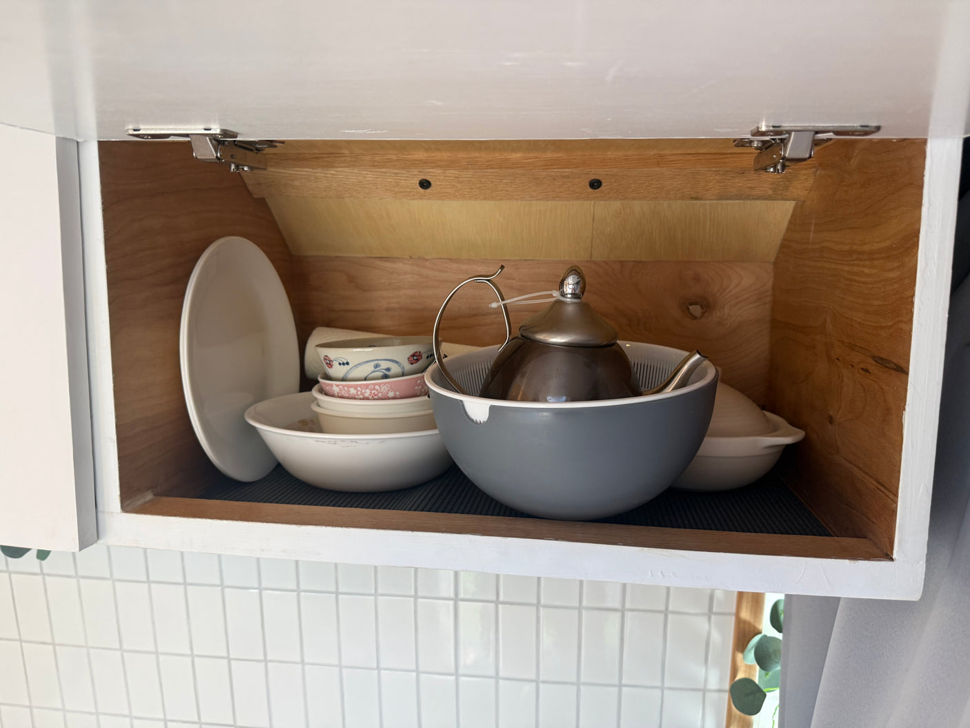 RV rental kitchen: compact cabinet storage with stacked plates, bowls, a colander, and a teapot.