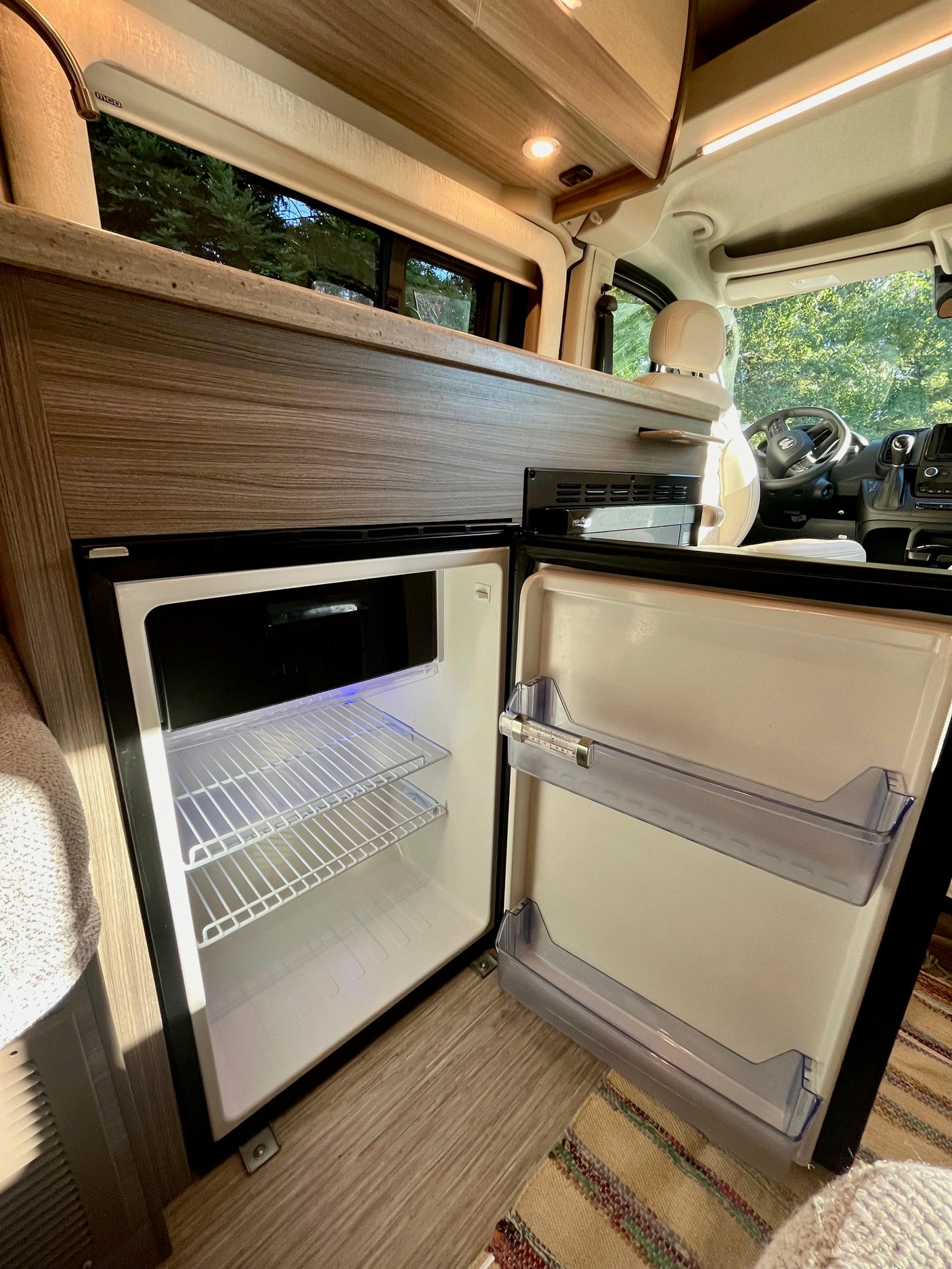 Interior of an RV rental with an open, compact fridge, perfect for storing food on your trip.