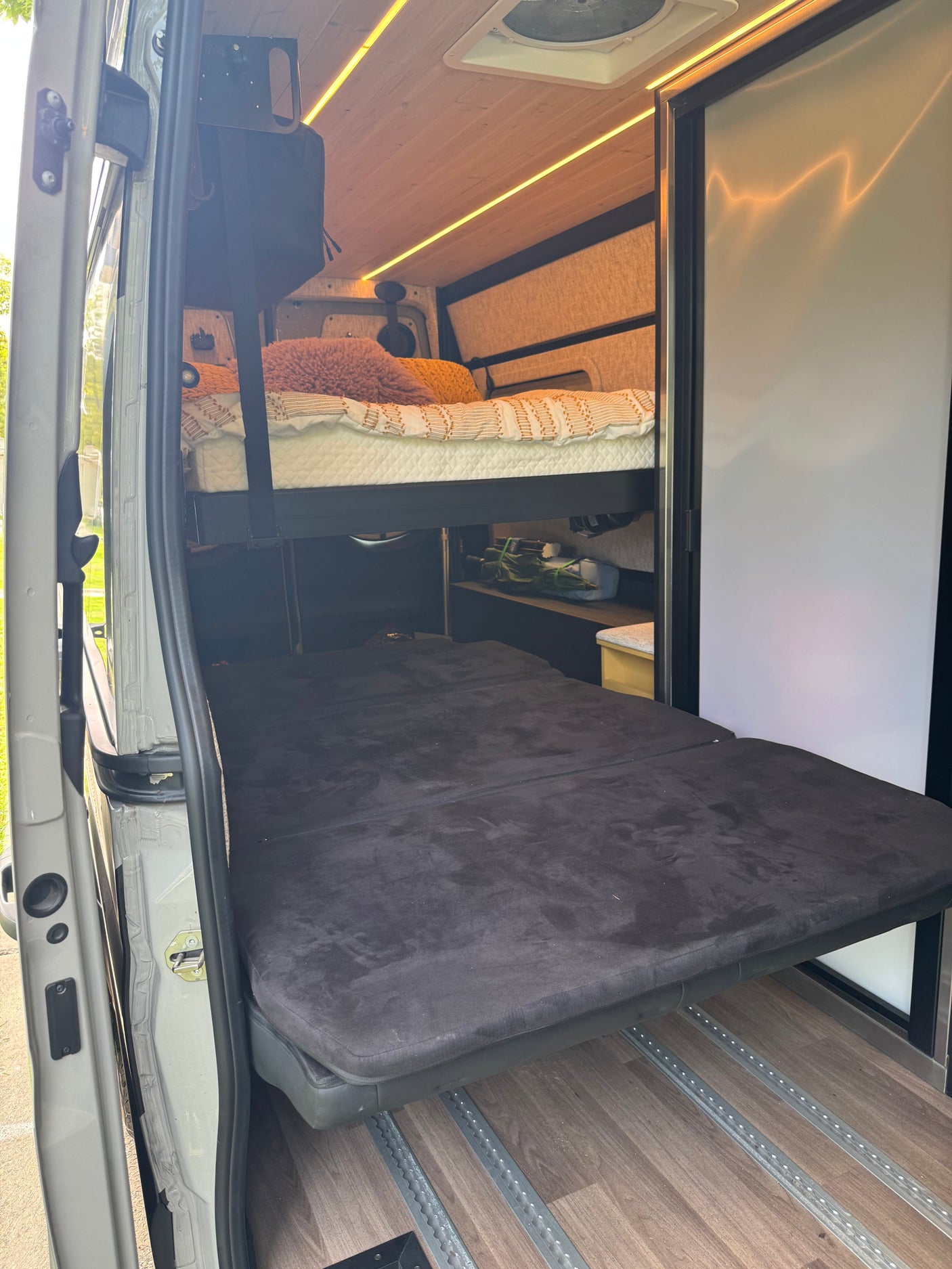 RV rental: Inside a camper van featuring a convertible lower bed, upper bunk, and wood-paneled ceiling with lights.