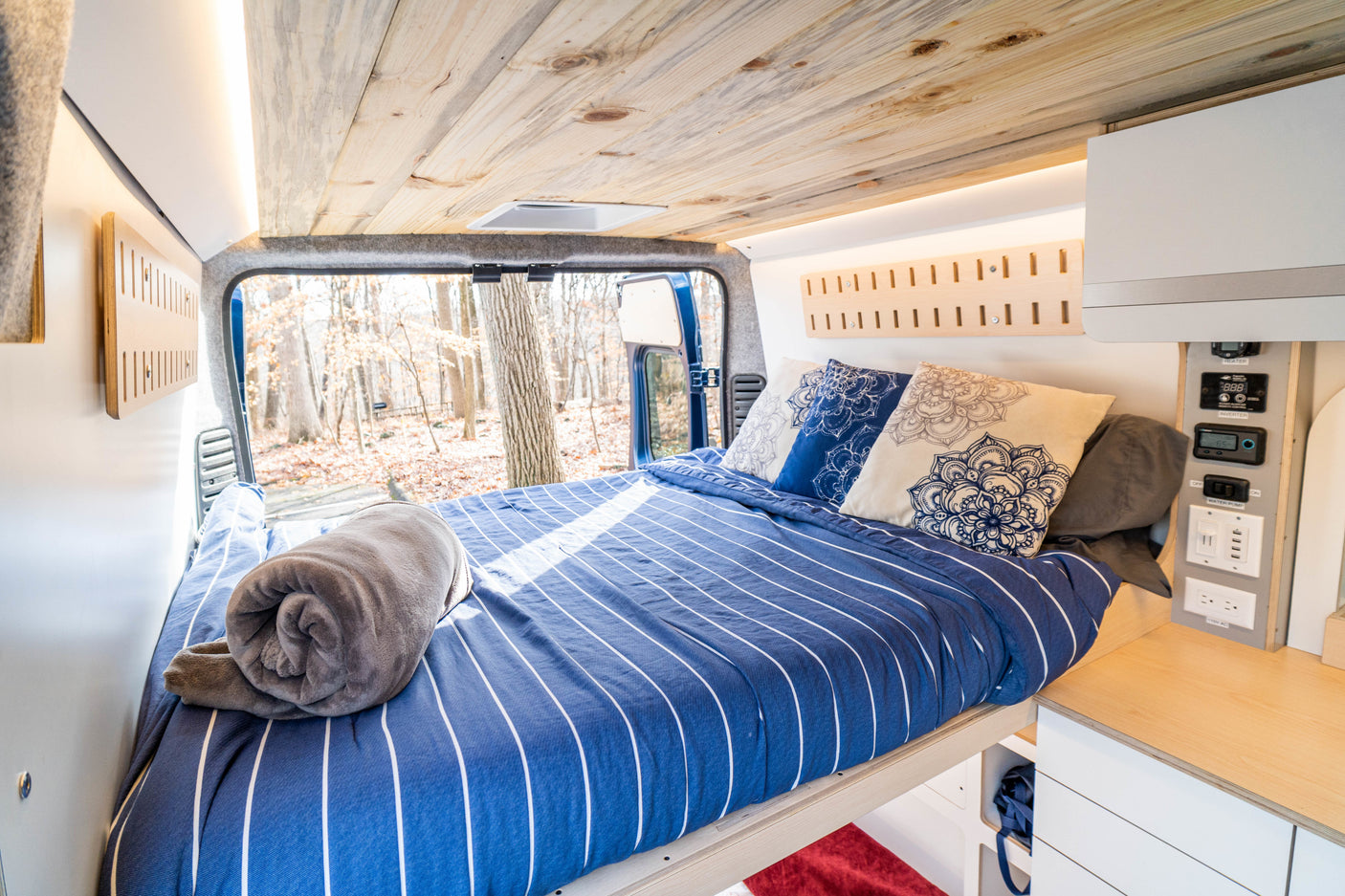 Inside a comfy RV rental: a modern camper van bedroom with striped bedding, wood ceiling, and control panel.