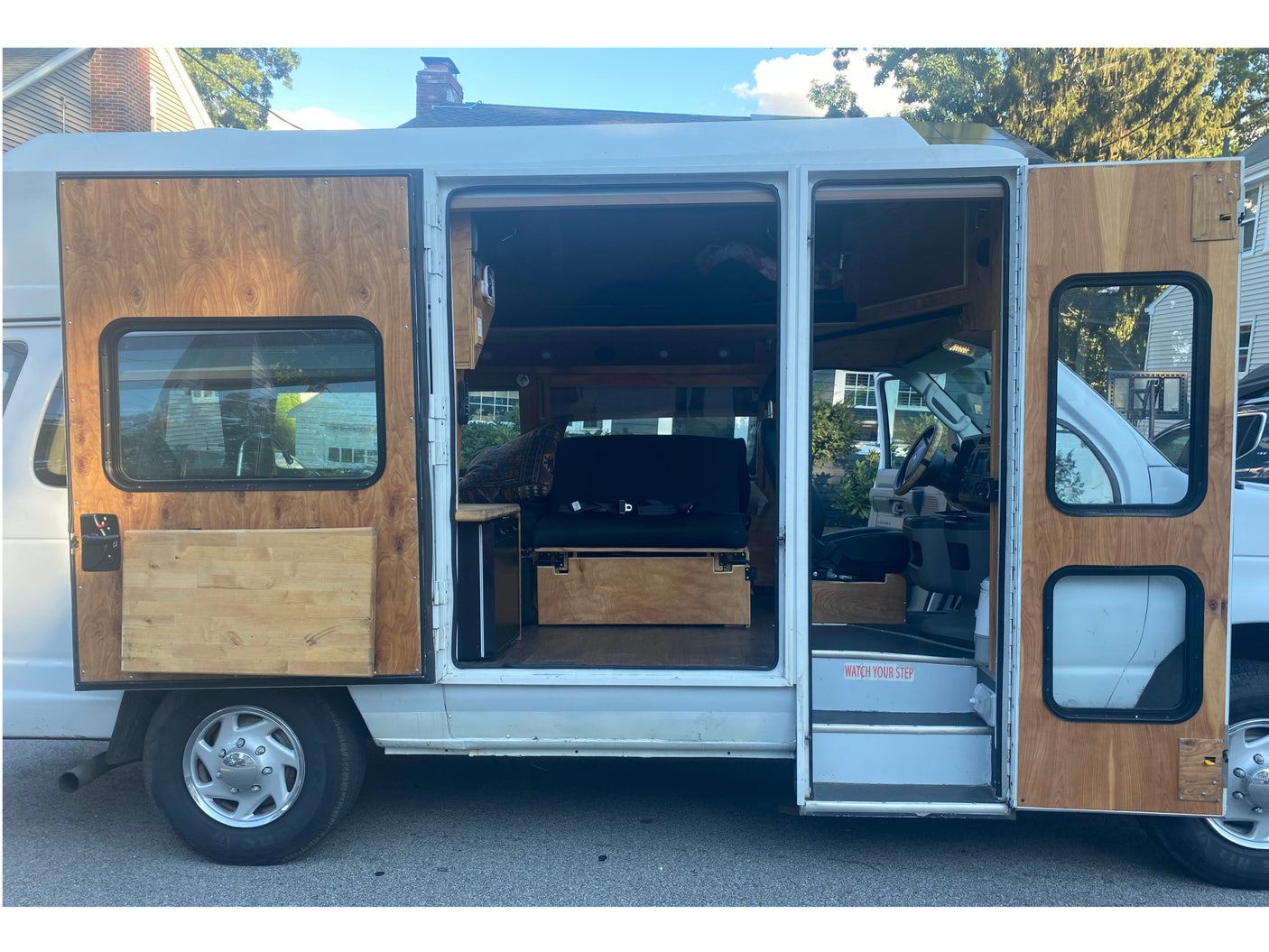 Detailed view of a white camper van's custom wooden interior, accessible through open side doors. Explore RV rental options!