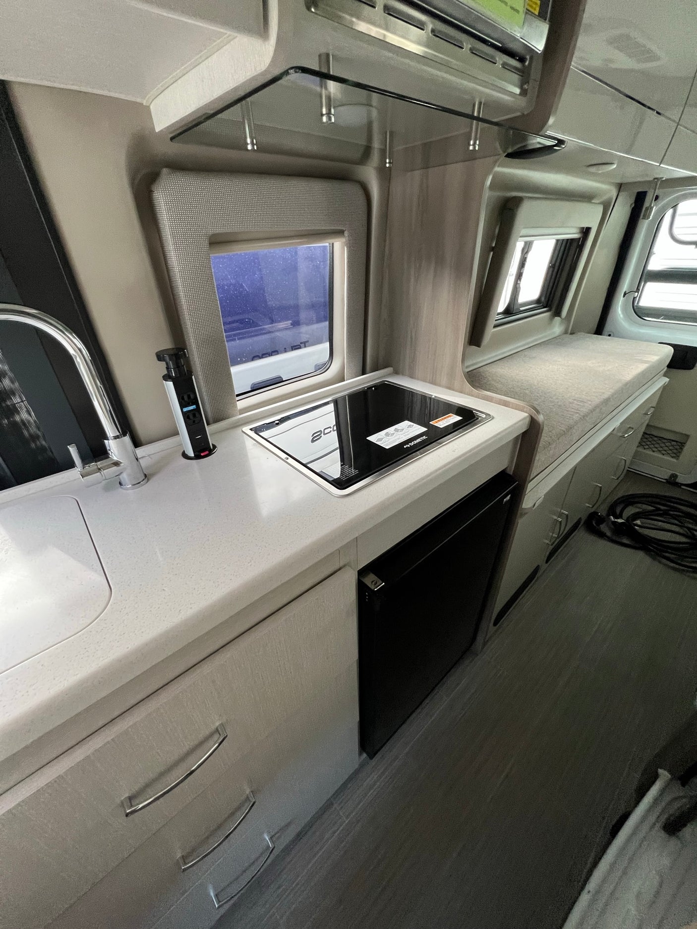 Experience an RV rental: Clean kitchenette with sink, cooktop, and fridge, integrated seating for convenience.