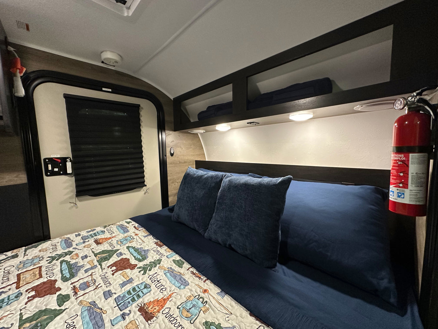 Cozy RV rental bedroom with a bed, camping quilt, and mounted fire extinguisher for safety and comfort.