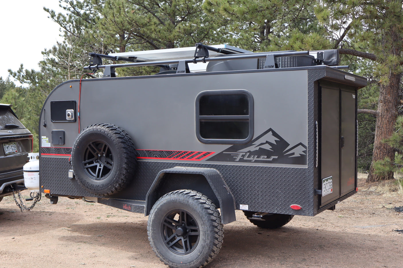 Gray off-road teardrop camper with solar panels, ideal for an rv rental adventure. Parked in a forest setting.