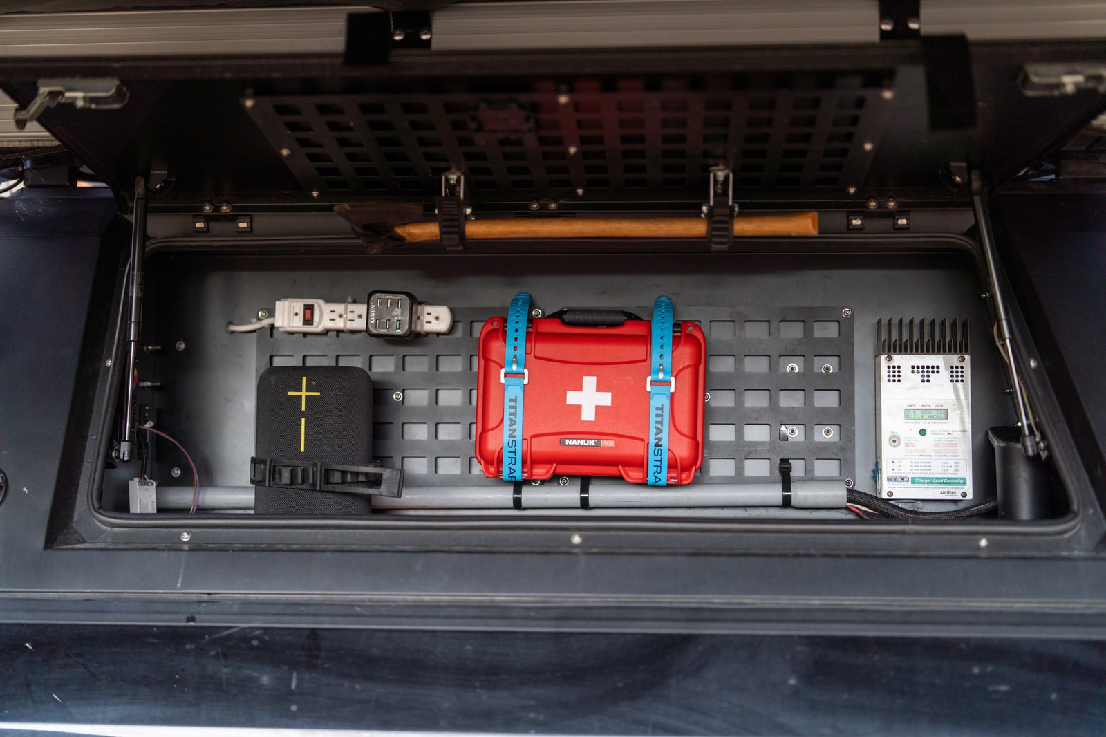 Optimized RV rental storage: a neatly organized compartment with first aid, electronics, axe, and solar charge controller.