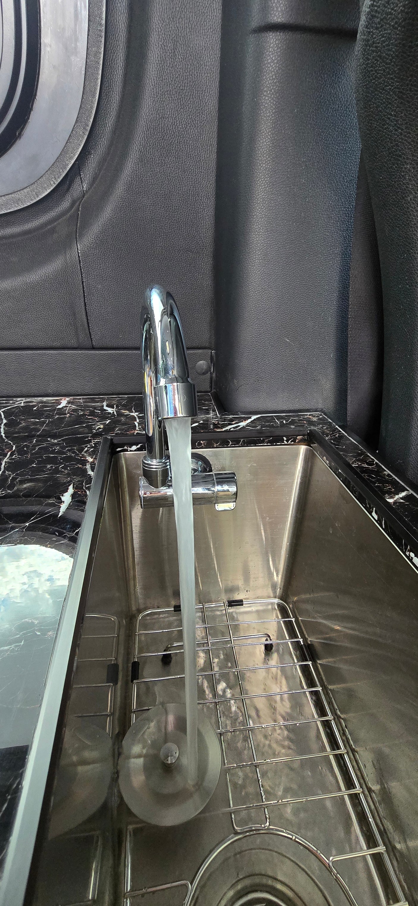 Functional RV rental kitchen: Running water flows from a chrome faucet into a stainless steel sink with a black marble countertop.