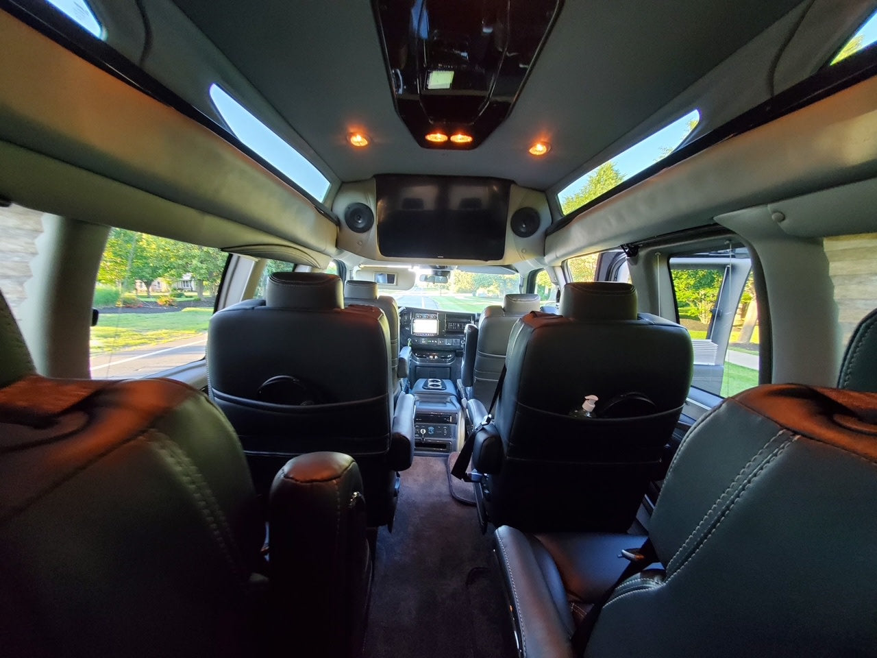 lush trees in background.|Front view of a sleek black high-top conversion van