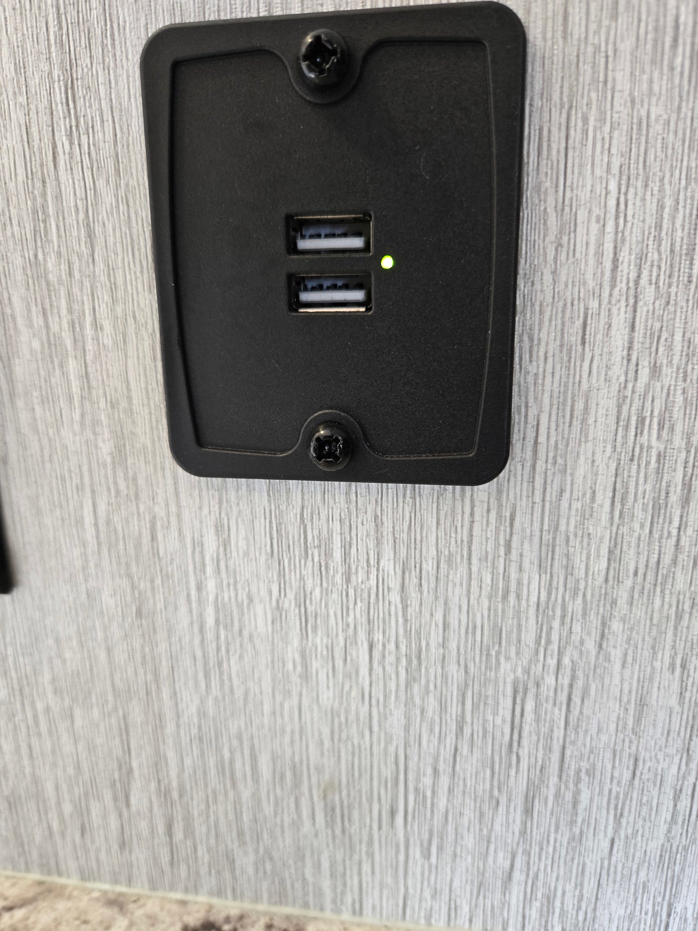 Dual USB charging station with a green LED, mounted on a wood-grain wall, useful in an rv rental.