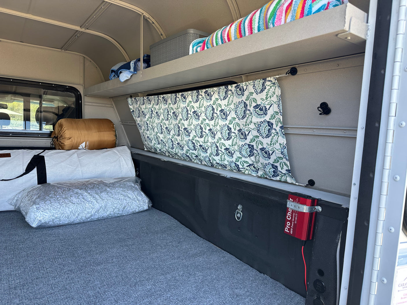 Cozy interior of an RV rental with a sleeping area, storage shelf, and power inverter for comfortable travel.