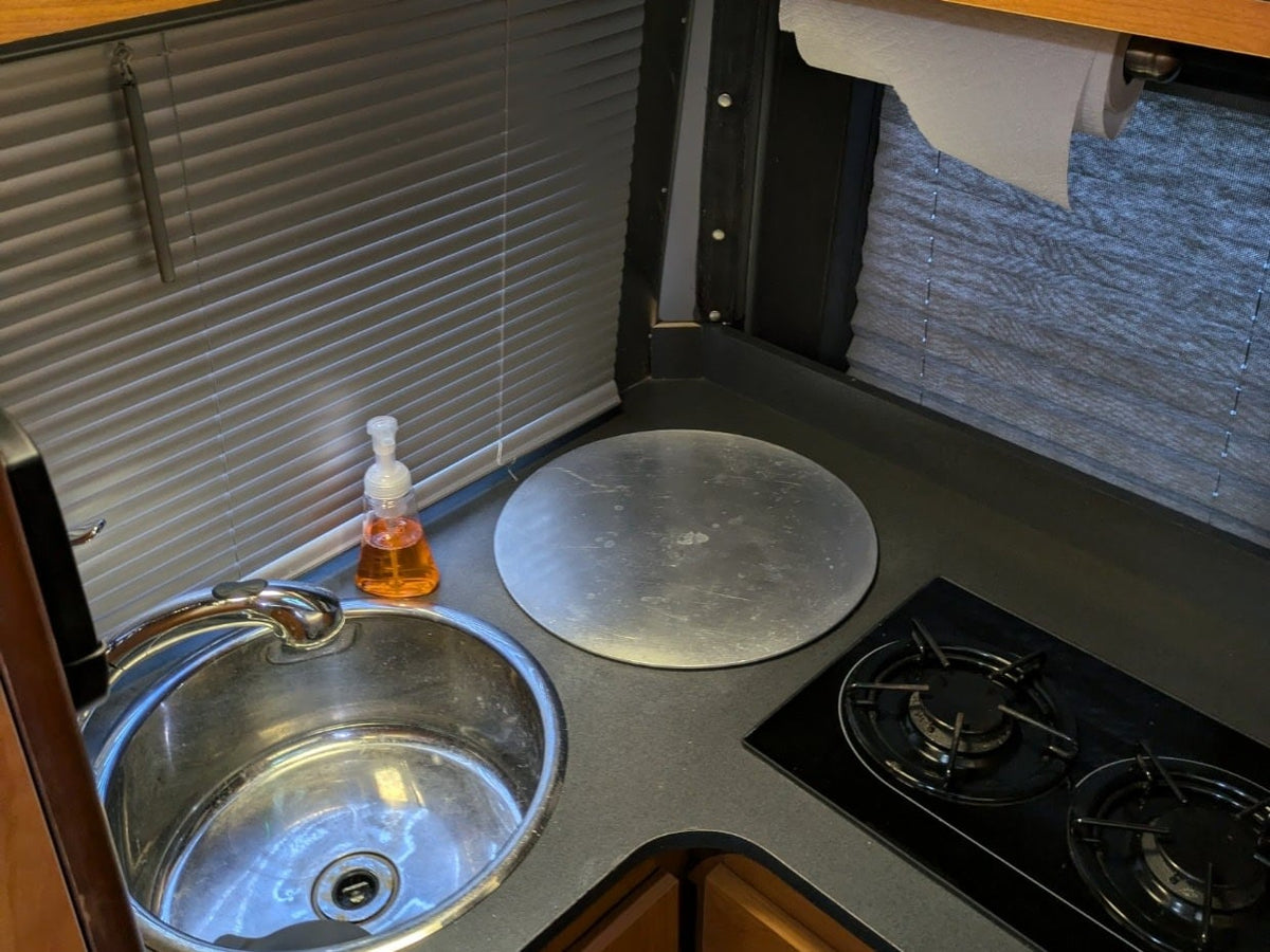backed by lush green hills under cloudy skies.|RV rental kitchen: stainless steel sink — photo 2