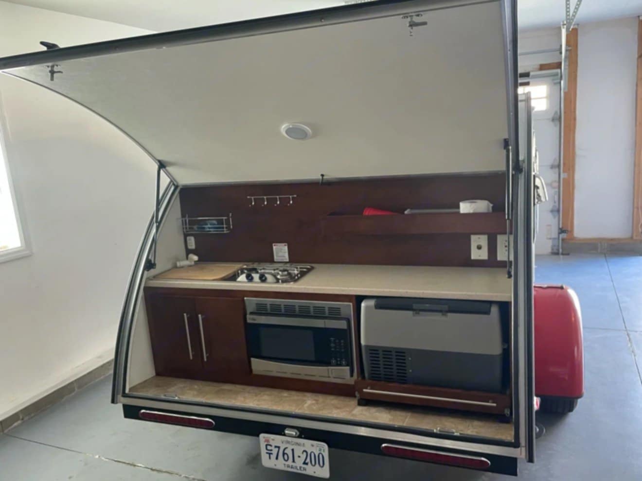 Compact teardrop camper outdoor kitchen, perfect for your next RV rental adventure! Features stove, sink, fridge, microwave.