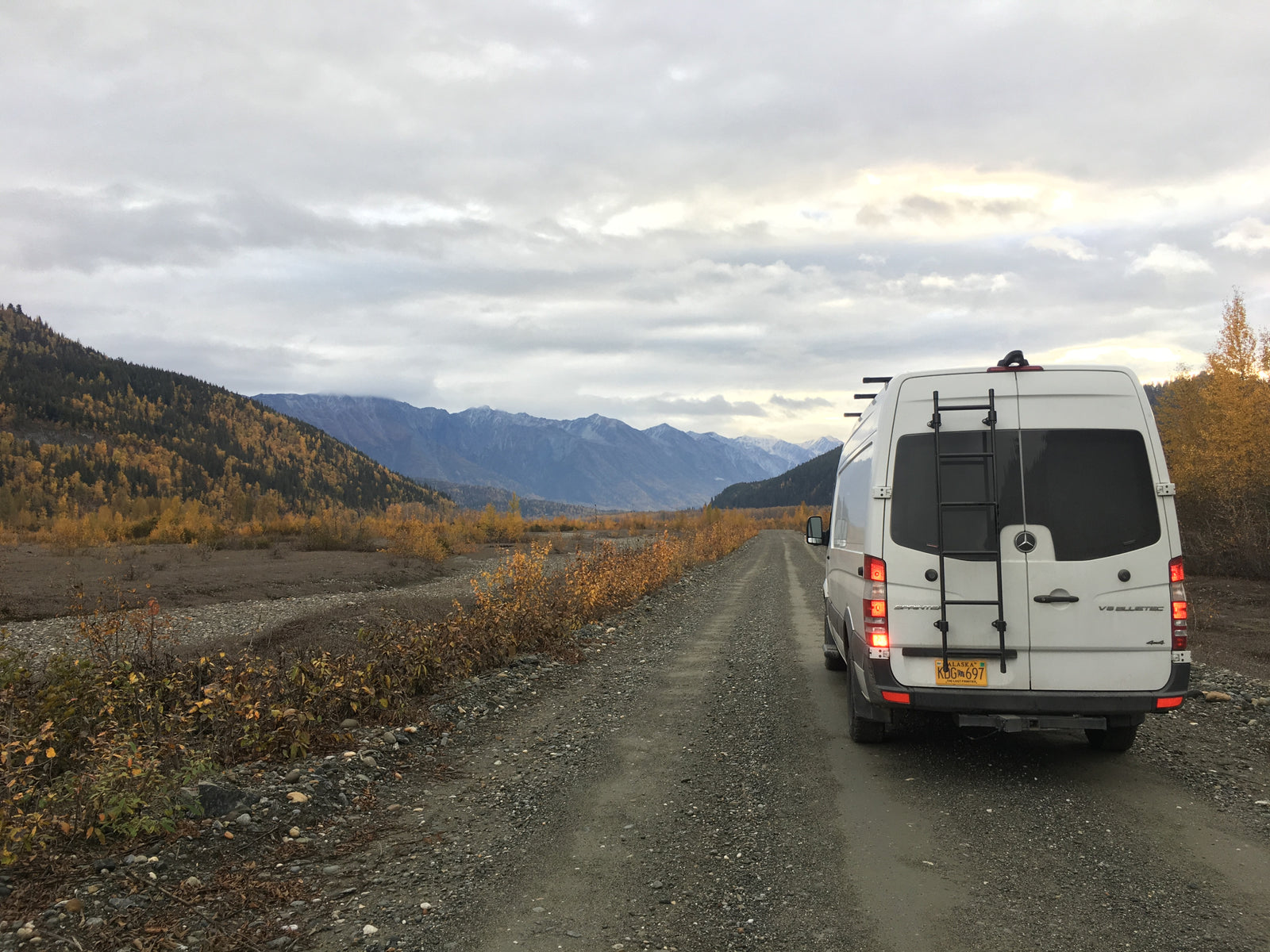 Adventurous rv rental: a white Sprinter van on a gravel road in Alaska's autumn mountains.