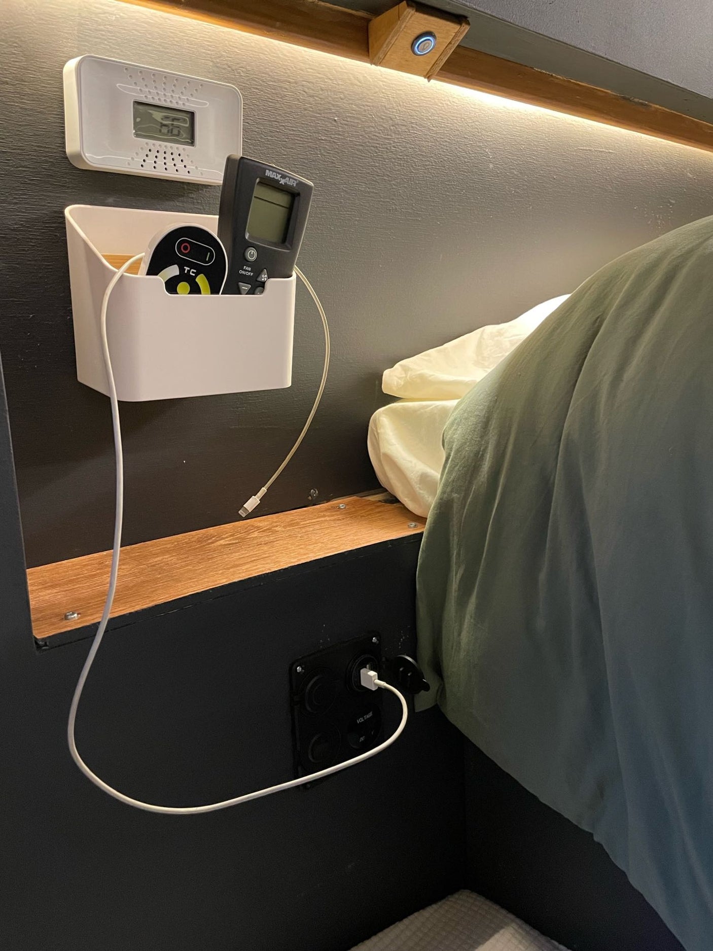Experience comfort in this rv rental. A cozy bunk features a digital monitor, fan remote, and USB charging. Ambient lighting creates a warm atmosphere.