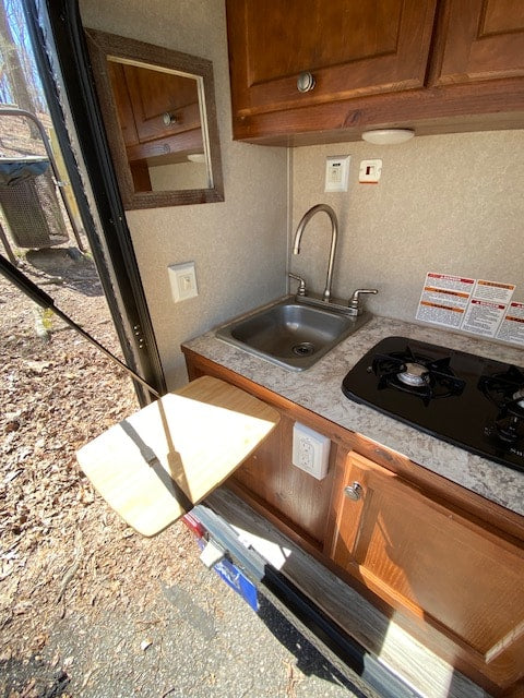 Compact RV rental kitchen with sink, stove, cabinets, and a convenient fold-out table for outdoor cooking access.