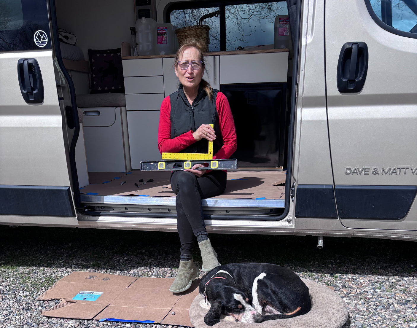 Prepping a Dave & Matt rv rental: woman leveling the interior while her dog rests beside the van.