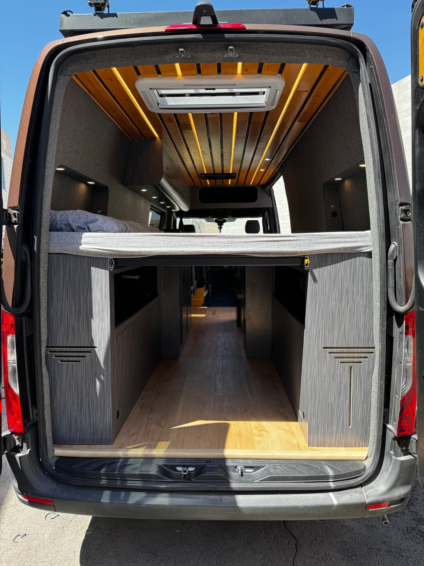 Explore this modern RV rental's custom camper van interior, showcasing a raised bed, wood ceiling, ambient lighting, and storage.