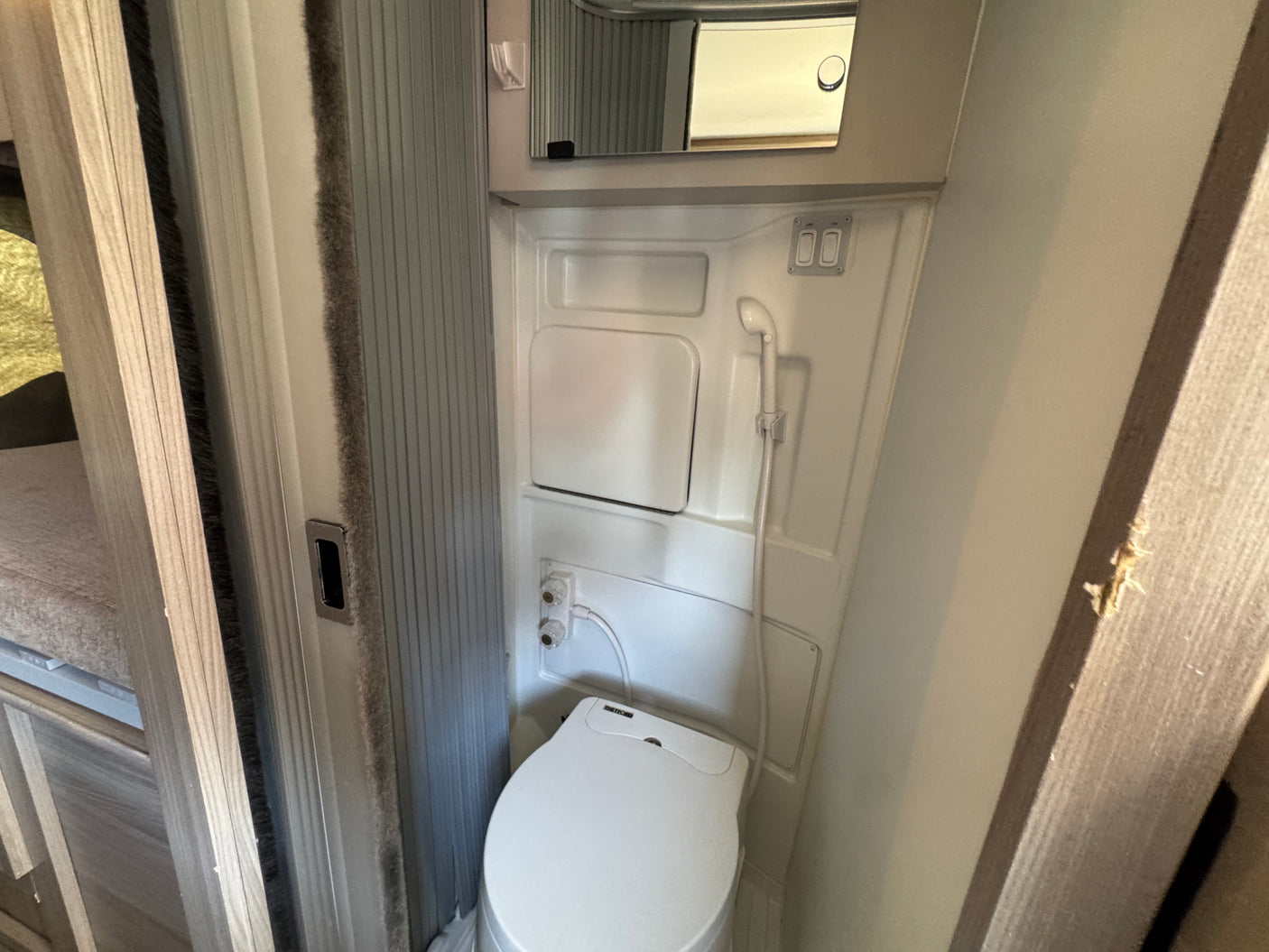 Compact RV rental bathroom featuring a white toilet, wall-mounted shower head, and small mirror above.