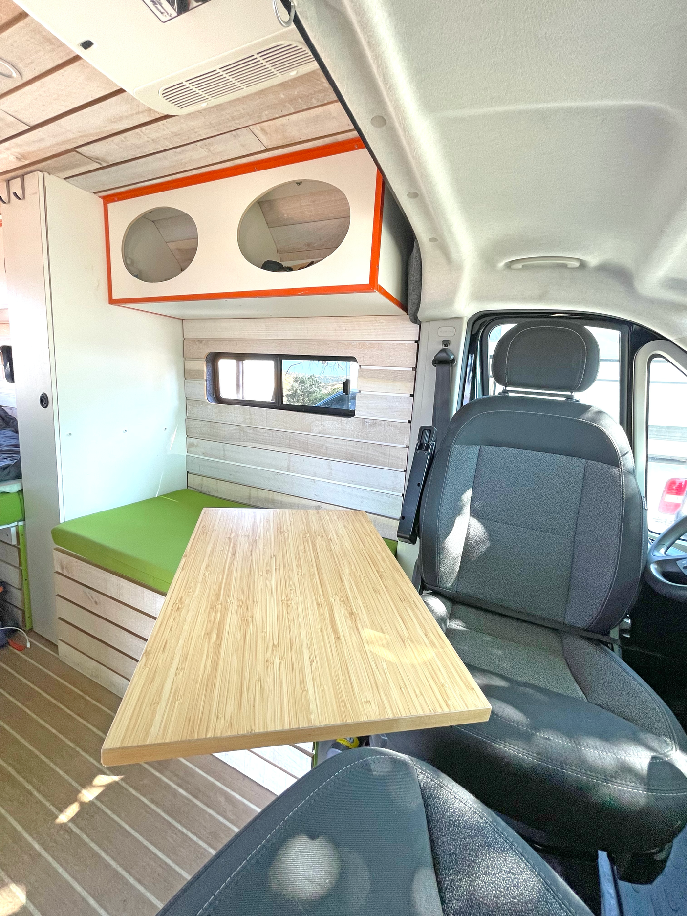 Inside a modern RV rental: light wood walls, green bench seat, and a bamboo table by the front passenger seat.