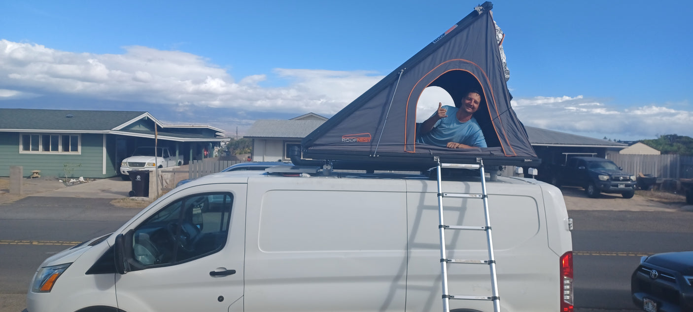 Happy man in a Roofnest rooftop tent atop a white van. Explore van camping with an RV rental for your next adventure!